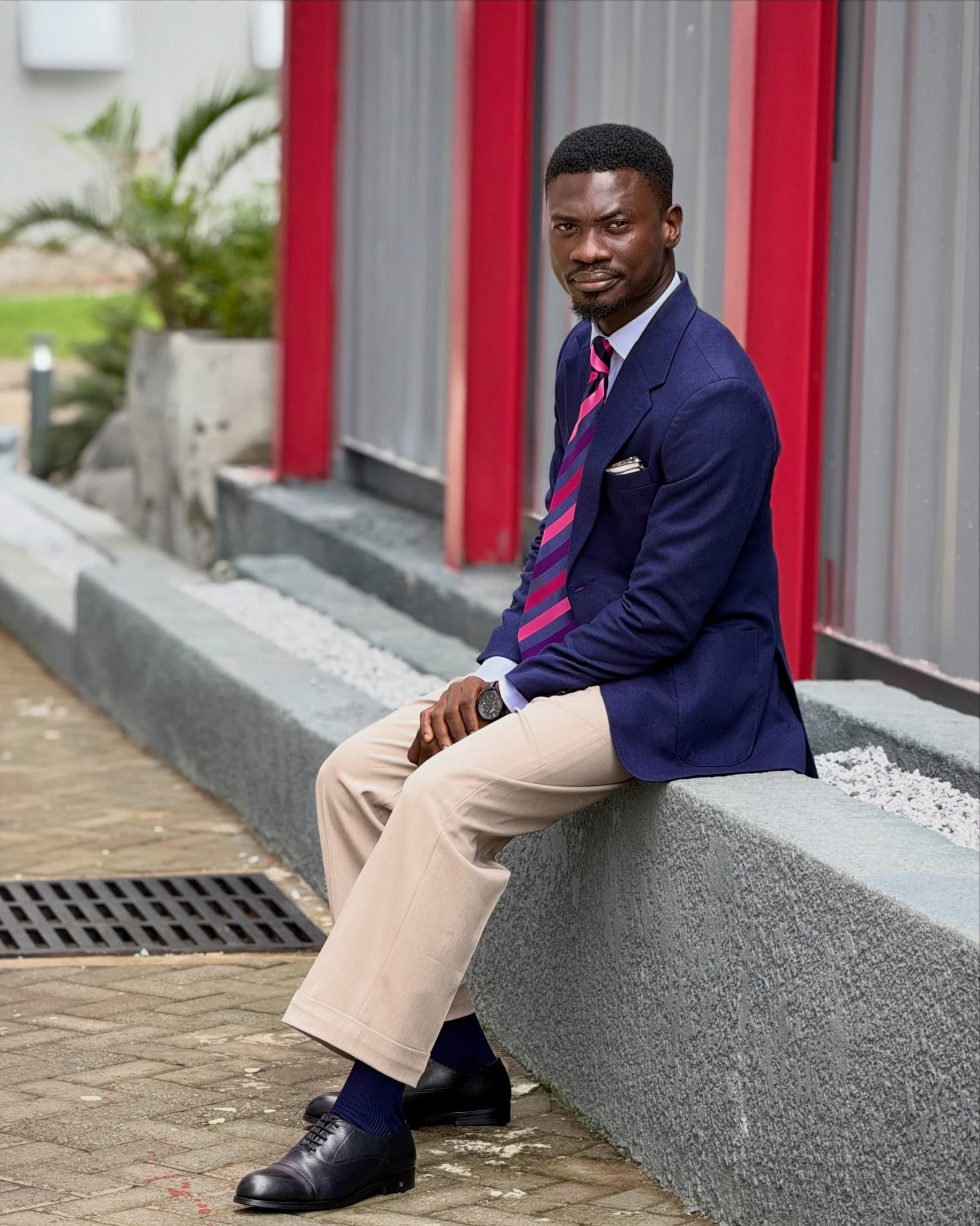 A man in a navy blazer seated on a wall, navy socks showing above black shoes