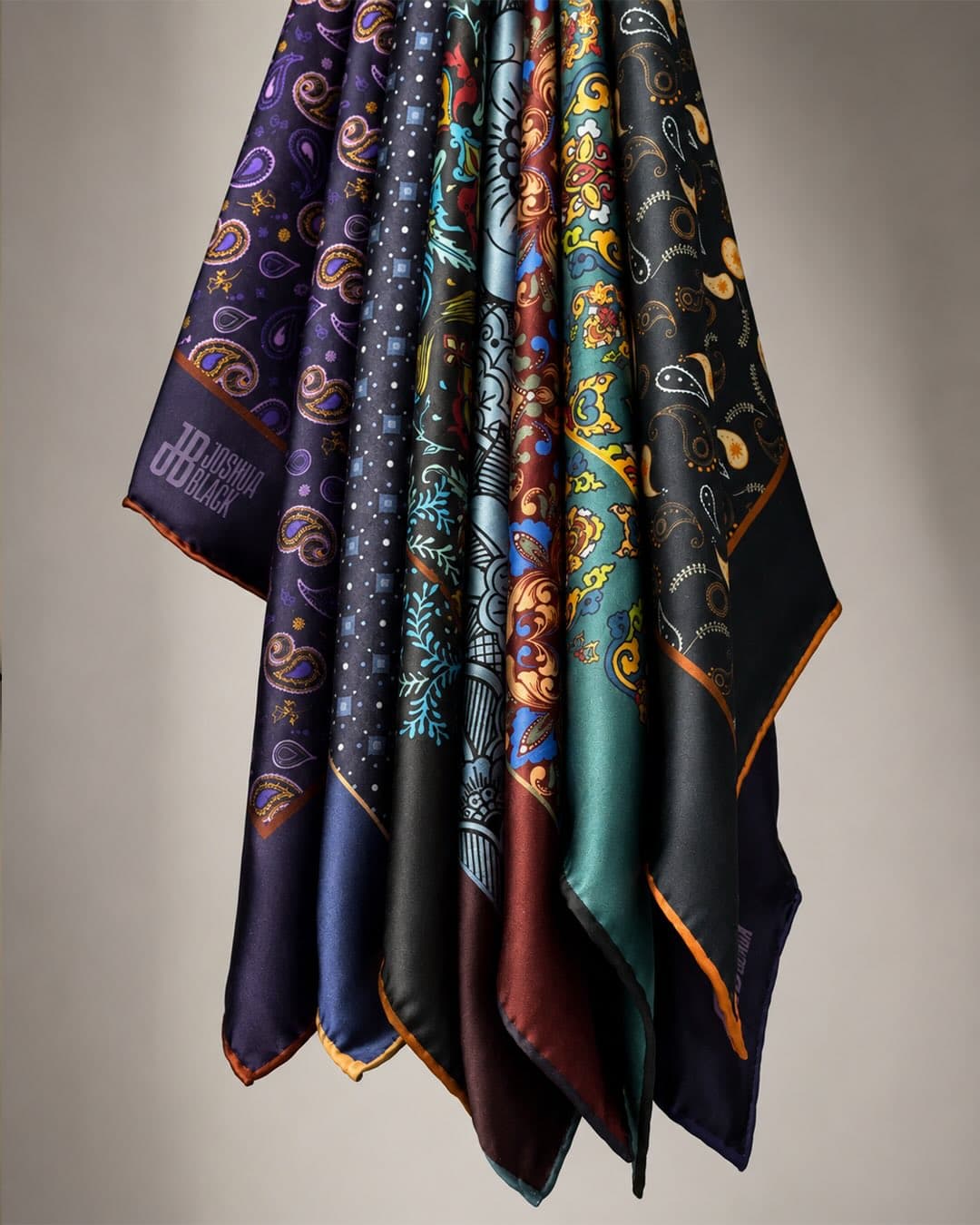 Pocket squares hanging together in folds of aubergine, navy, slate, oxblood, emerald and black