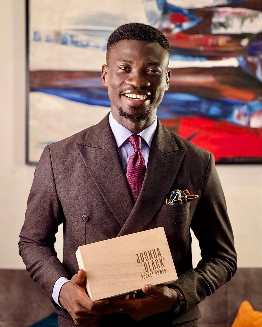 Opeyemi Okediji in a brown double-breasted suit, holding a Pocket Power box