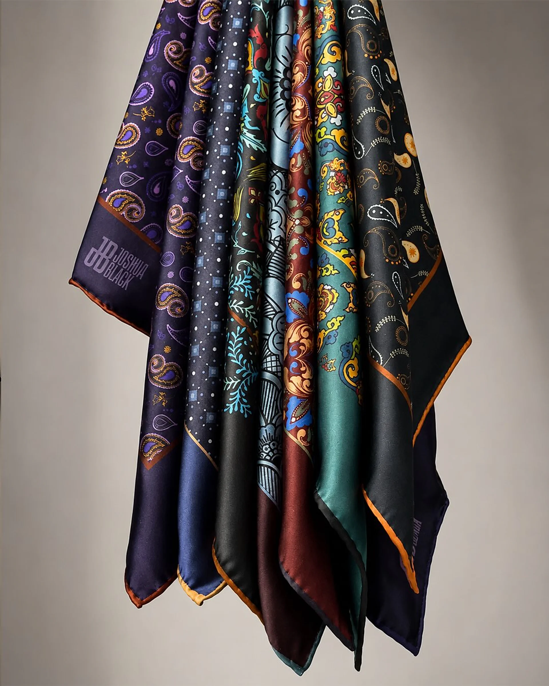 Pocket squares hanging together in folds of aubergine, navy, slate, oxblood, emerald and black